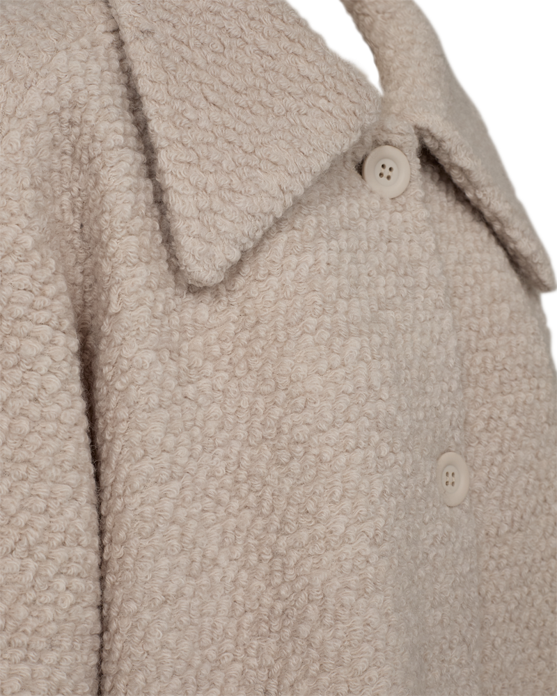Close-up of the FQSIXTY beige Jacke featuring a textured, curly wool pattern. It includes a wide collar and white button fastening, with its weite Passform enhancing the fabric’s soft and cozy look.