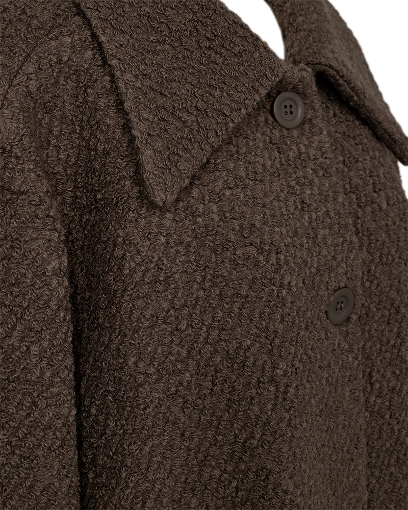 Close-up of the FQSIXTY Jacke in brown with a wide collar and two visible front buttons. The fabric, showcasing a geprägte Qualität, looks warm and thick, perfect for cooler weather.